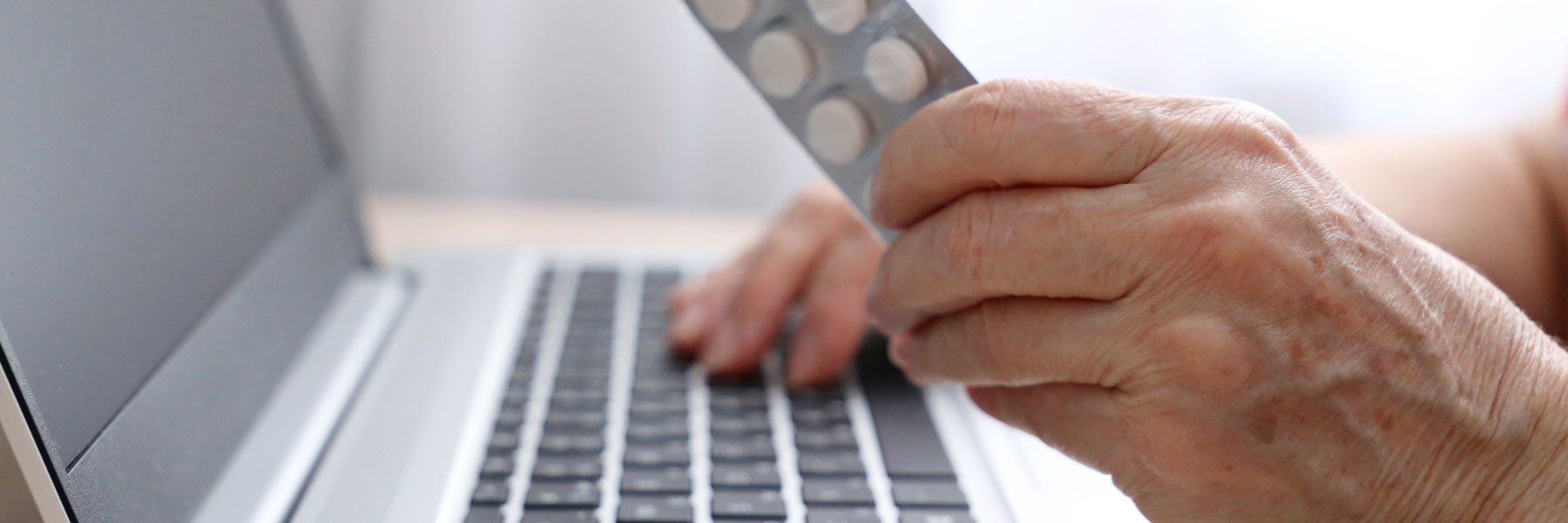 Elderly person with prescription typing on laptop